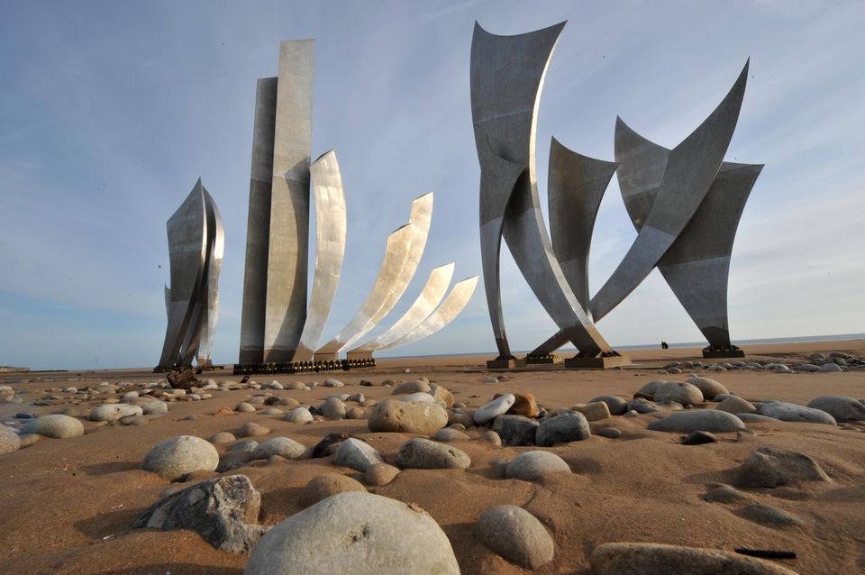 Monumento di metallo moderno su una spiaggia, circondato da ciottoli, che rappresentano la storia delle spiagge di atterraggio.