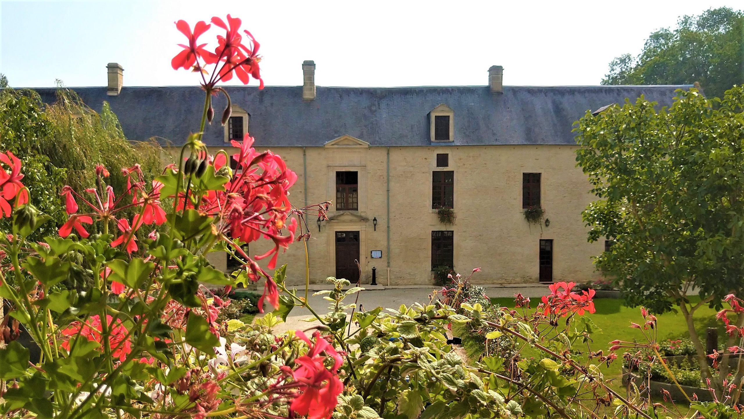 Vista del maniero di Mathan a Crépon, con fiori colorati in primo piano e un edificio storico sullo sfondo.