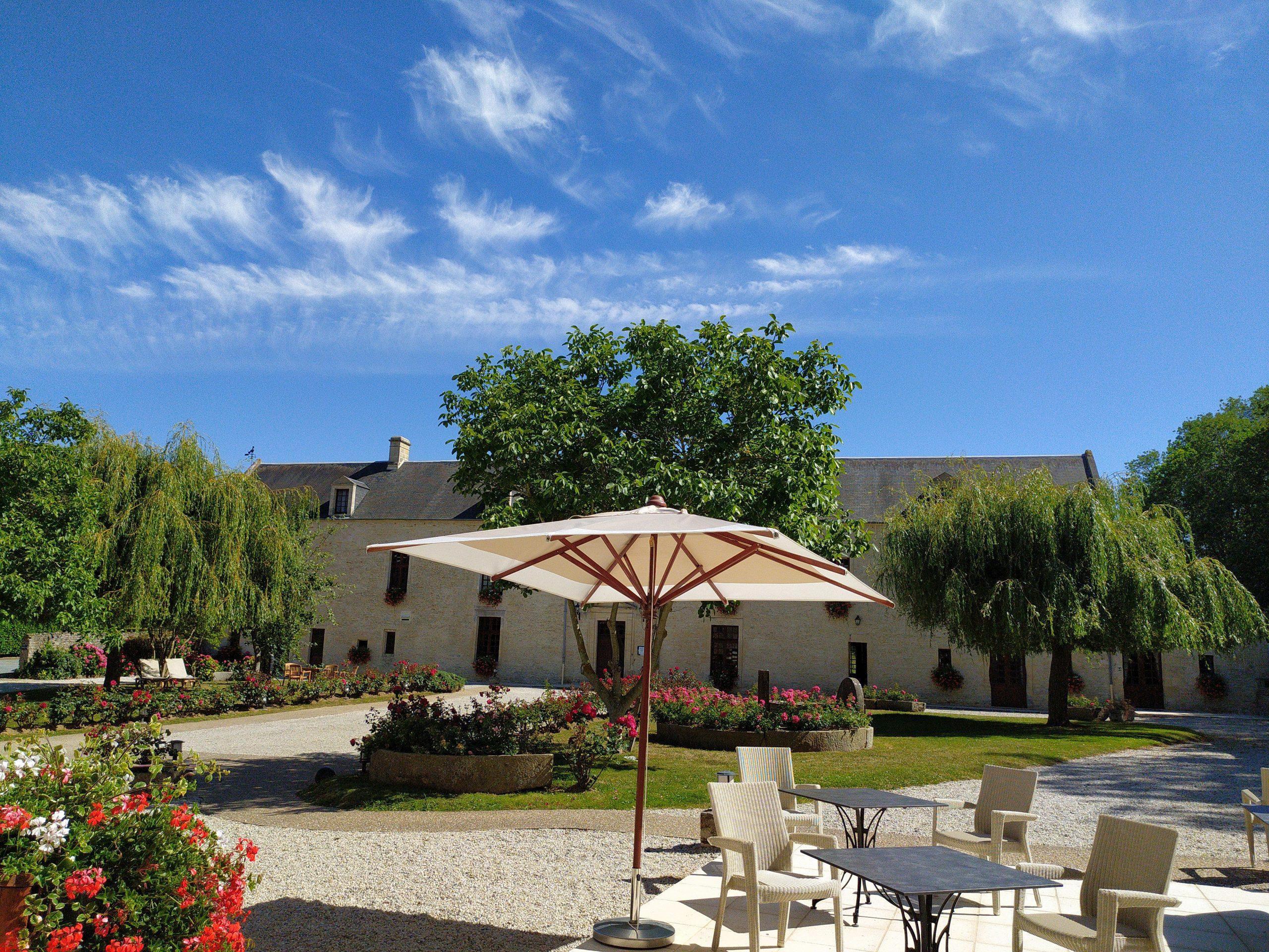 Vista del maniero di Mathan con il suo cortile, il parasole e i giardini fioriti sotto un cielo blu.