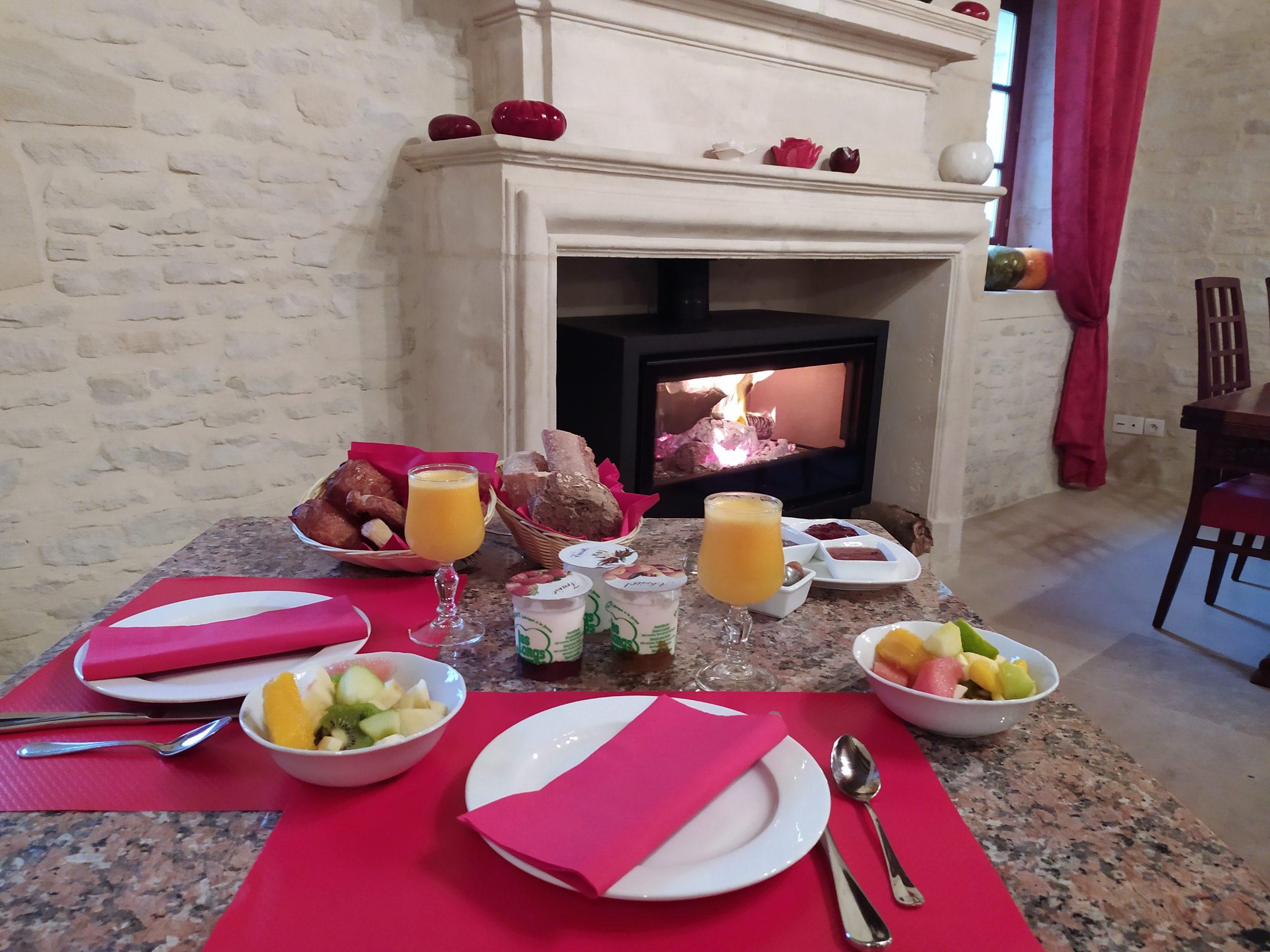 Elegante desayuno con frutas, pasteles y jugos, cerca de una chimenea en un entorno cálido.