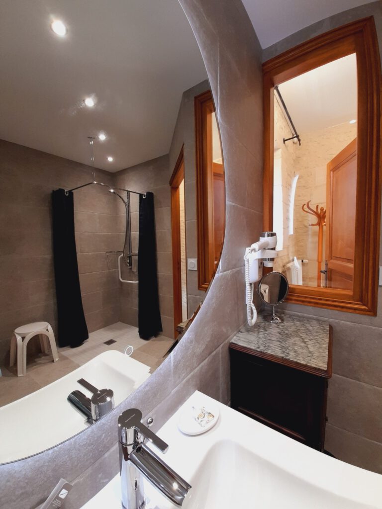 Elegante bagno di una suite Junior Triple PMR, con doccia accessibile, specchio e lavandino moderno.