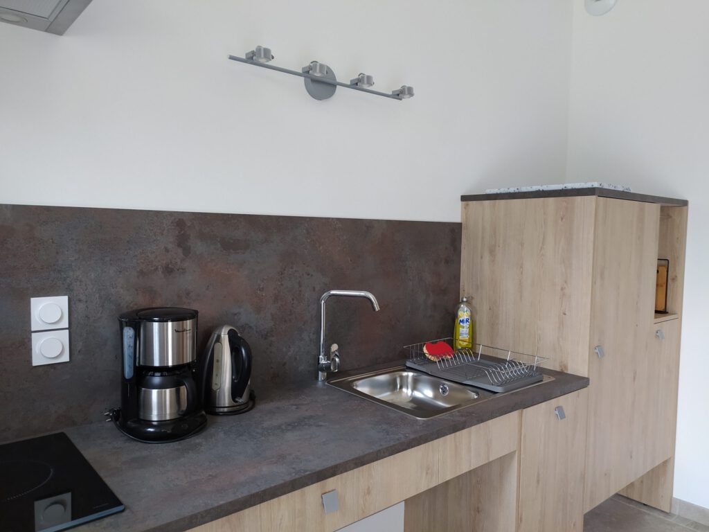 Cucina montata in una suite Junior Triple PMR, con lavandino, caffettiera, bollitore ed elegante spazio di archiviazione.