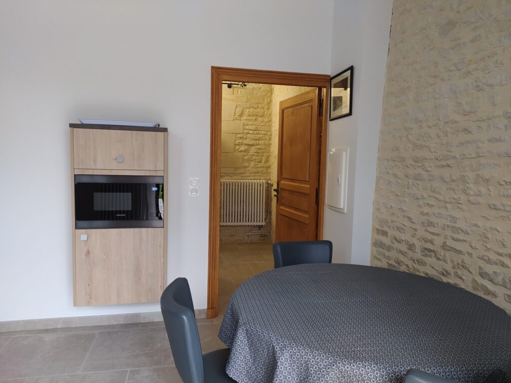 Vista interna di una suite Junior Triple PMR con mobili moderni e accesso a un bagno, muri di pietra a vista.