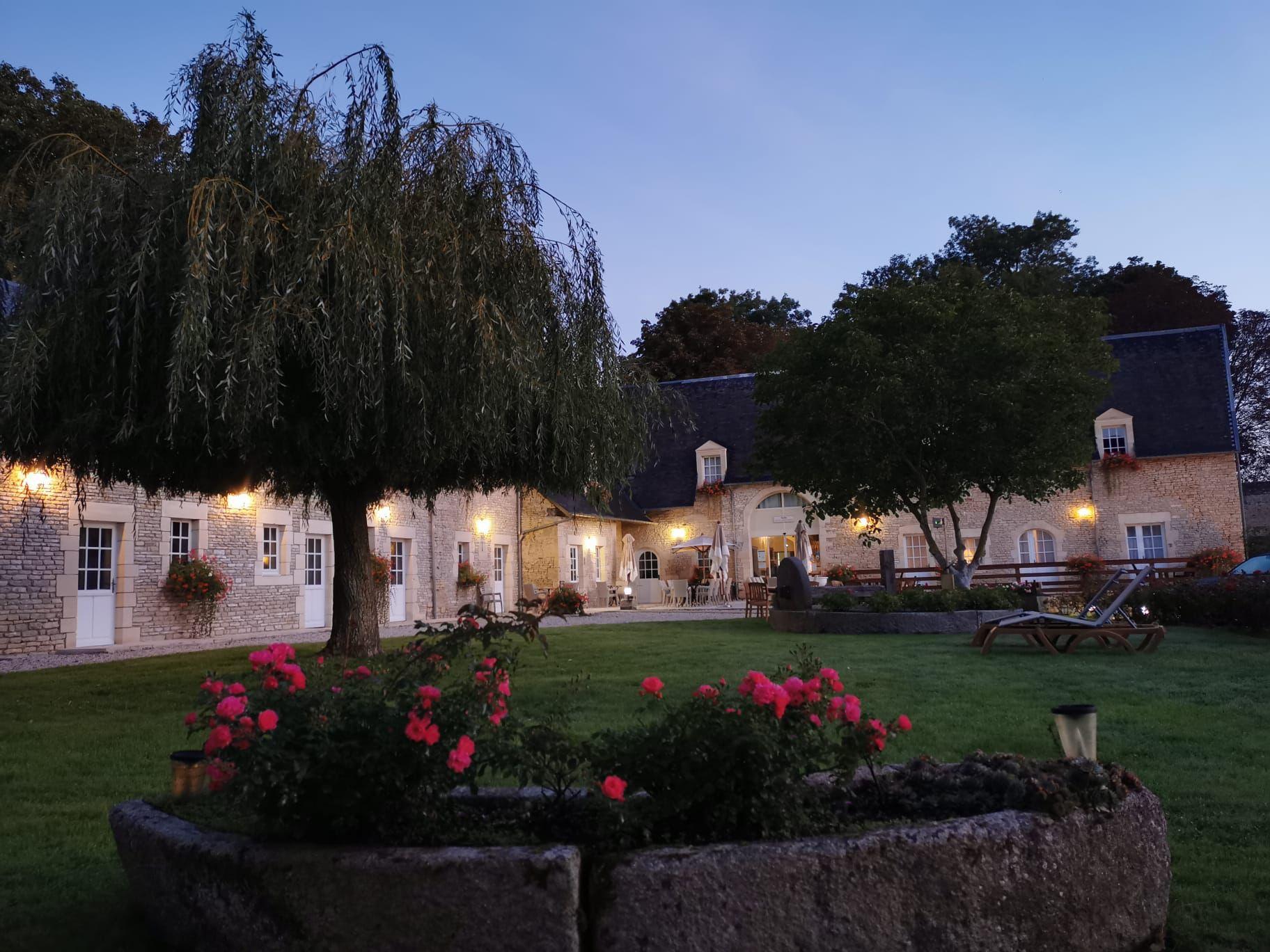 Udsigt til Mathan Manor i Crépon, omgivet af en grøn park og en gårdhave, oplyst med skumring.