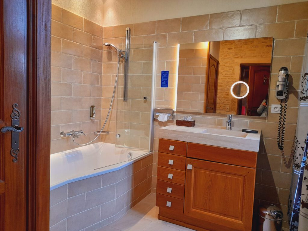 Bagno elegante con vasca, doccia in vetro, mobili in legno e specchio leggero. Atmosfera moderna e calda.