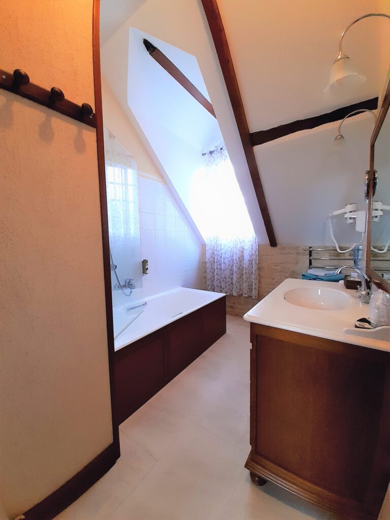 Bagno elegante con vasca, bacino di legno e luce naturale, in un ambiente storico e caldo.