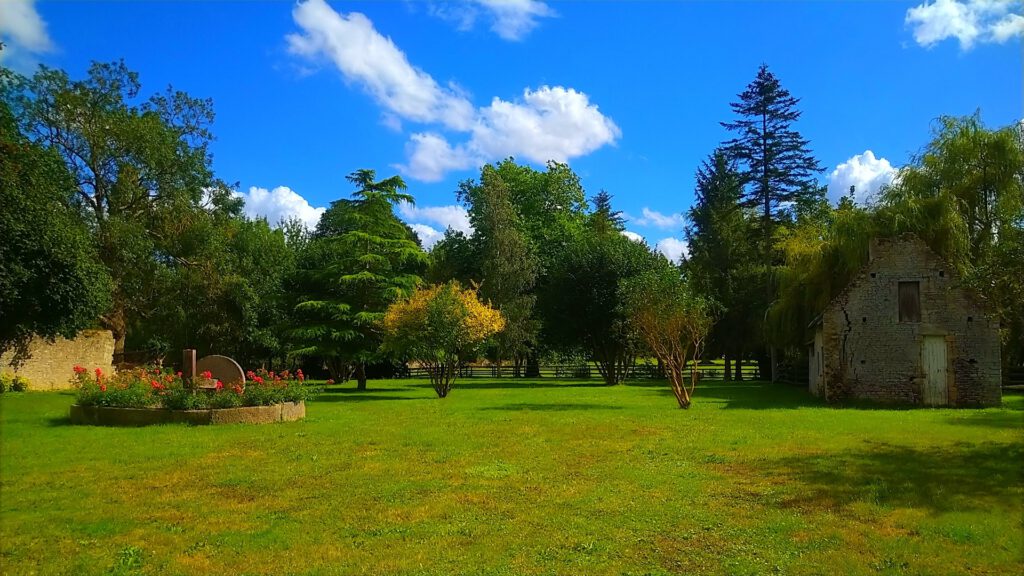 Vasto parco verde che circonda un vecchio edificio, sotto un cielo blu punteggiato di nuvole.