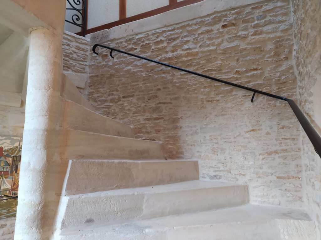 Scade in pietra in uno spazio storico, con rampa di metallo e pareti in pietra a vista.