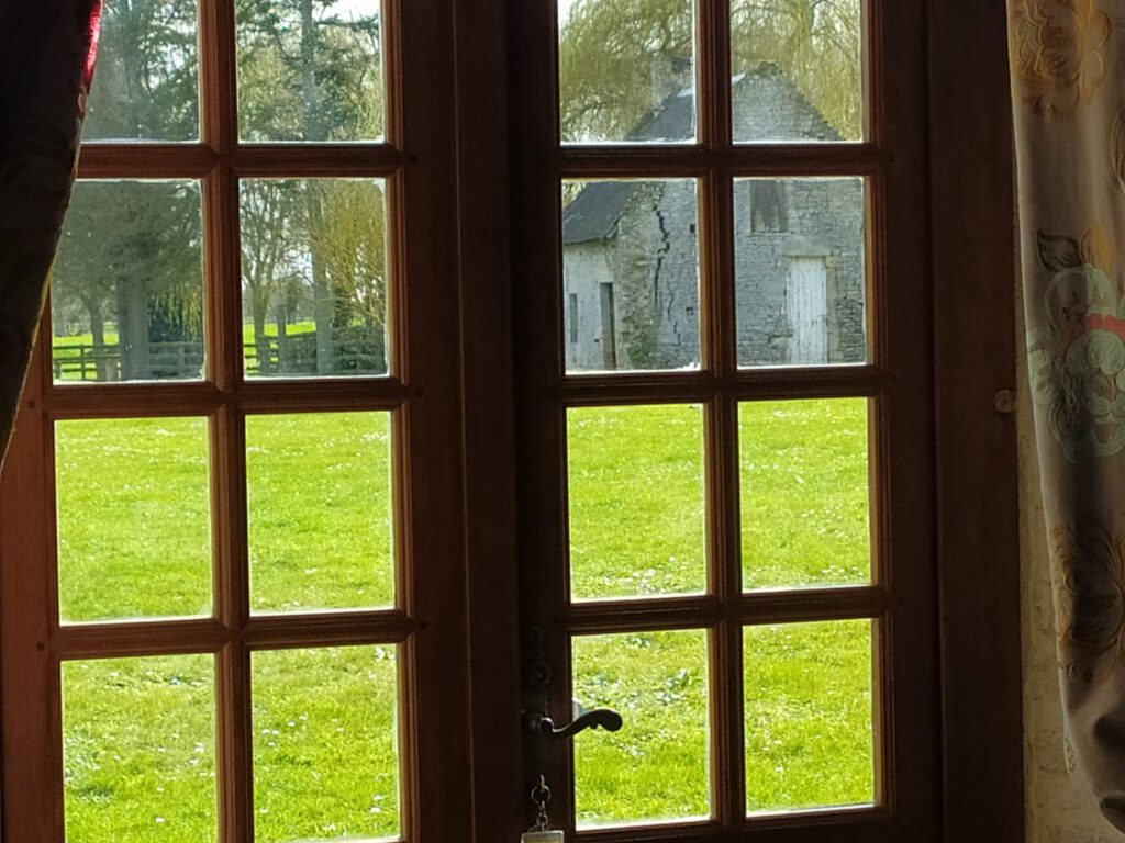 Guarda attraverso una finestra di un appartamento nel Mathan Manor, che mostra un parco verde e un vecchio edificio in pietra.