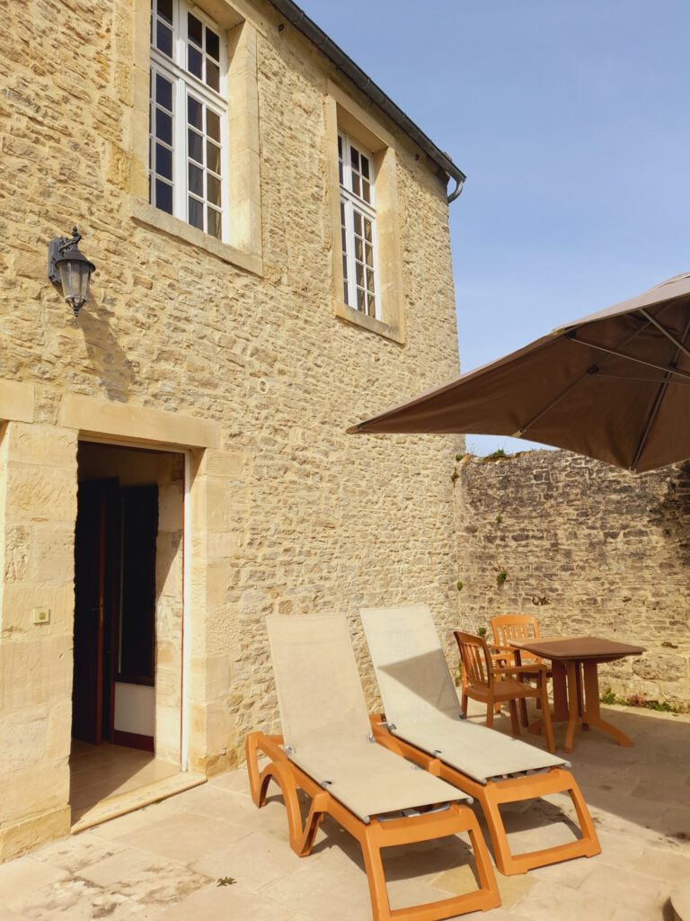Terrazza con padiglioni e tavolo in legno, davanti a una facciata in pietra dal maniero di Mathan, sotto un cielo limpido.