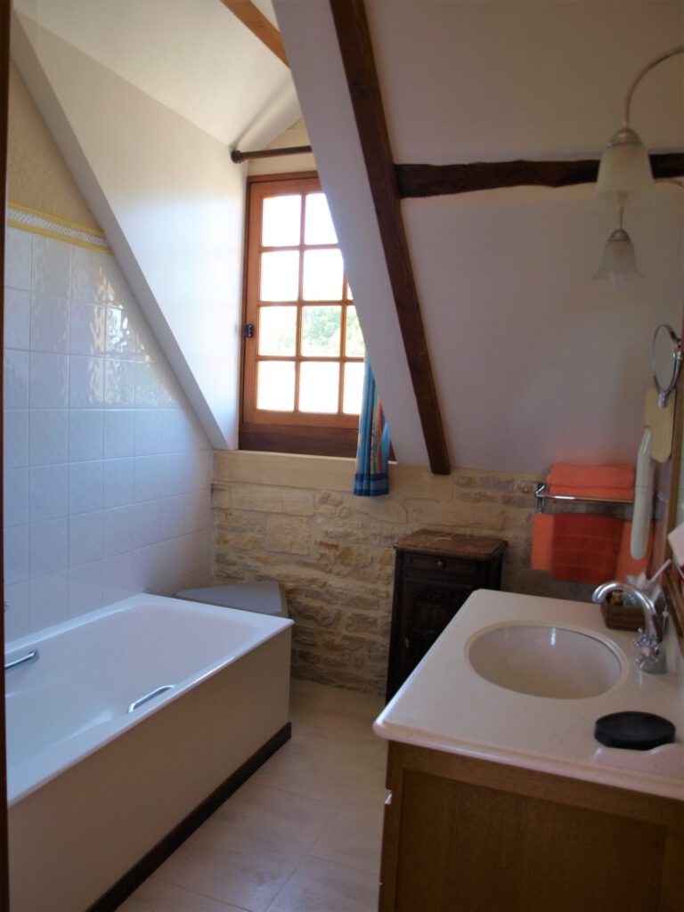 Bagno elegante con vasca, finestra in legno e muri di pietra, offrendo un&#39;atmosfera calda e rilassante.