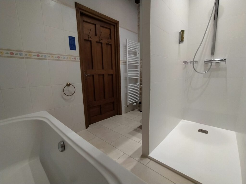 Baño moderno con bañera y ducha separada, azulejos ligeros y elegante puerta de madera.