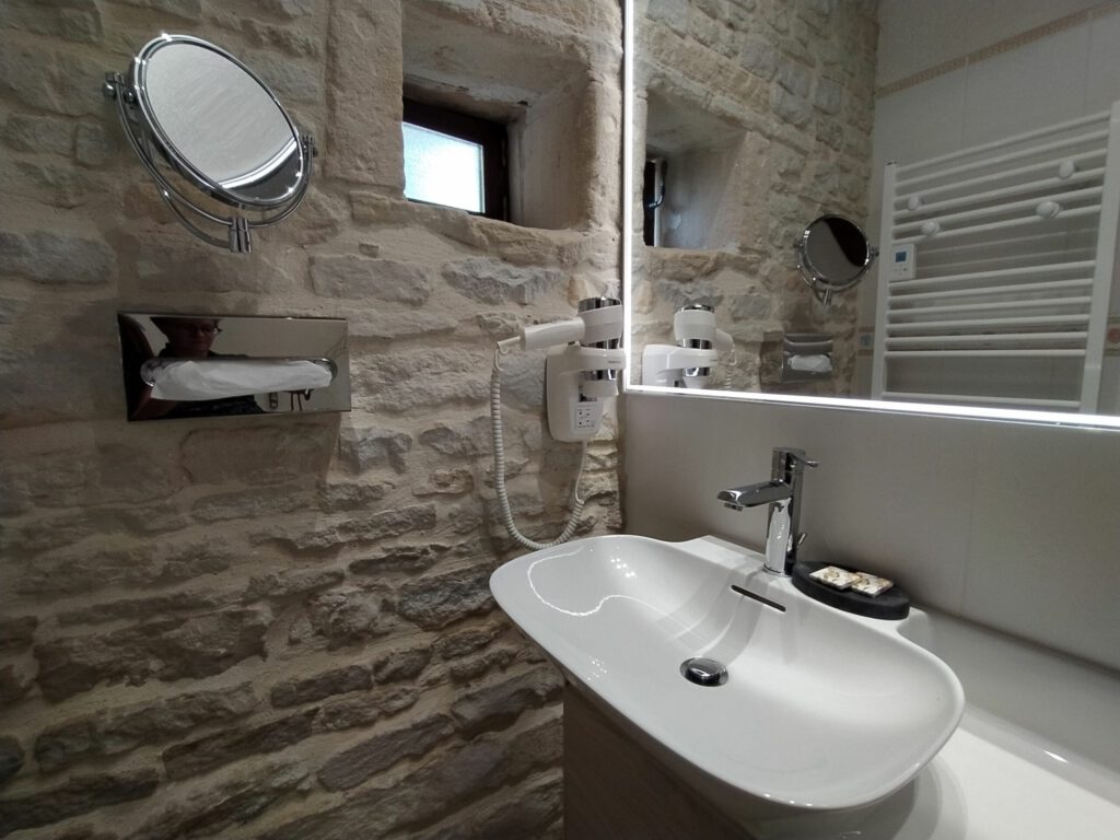 Baño moderno con fregadero de porcelana, espejo encendido y paredes de piedra expuestas.