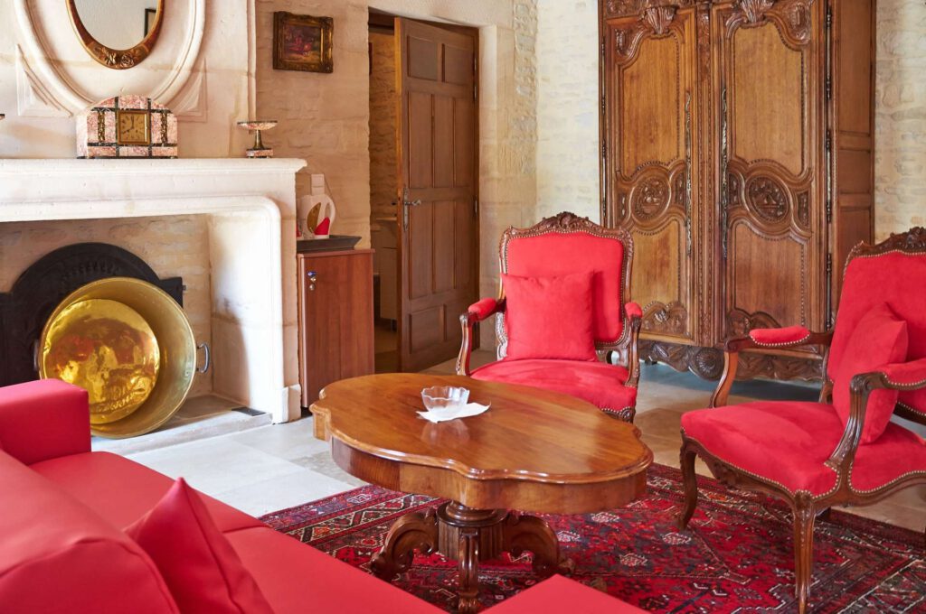 Interiør af Mathan Manor, med en elegant stue, røde lænestole, et træbord og en stenpejs.