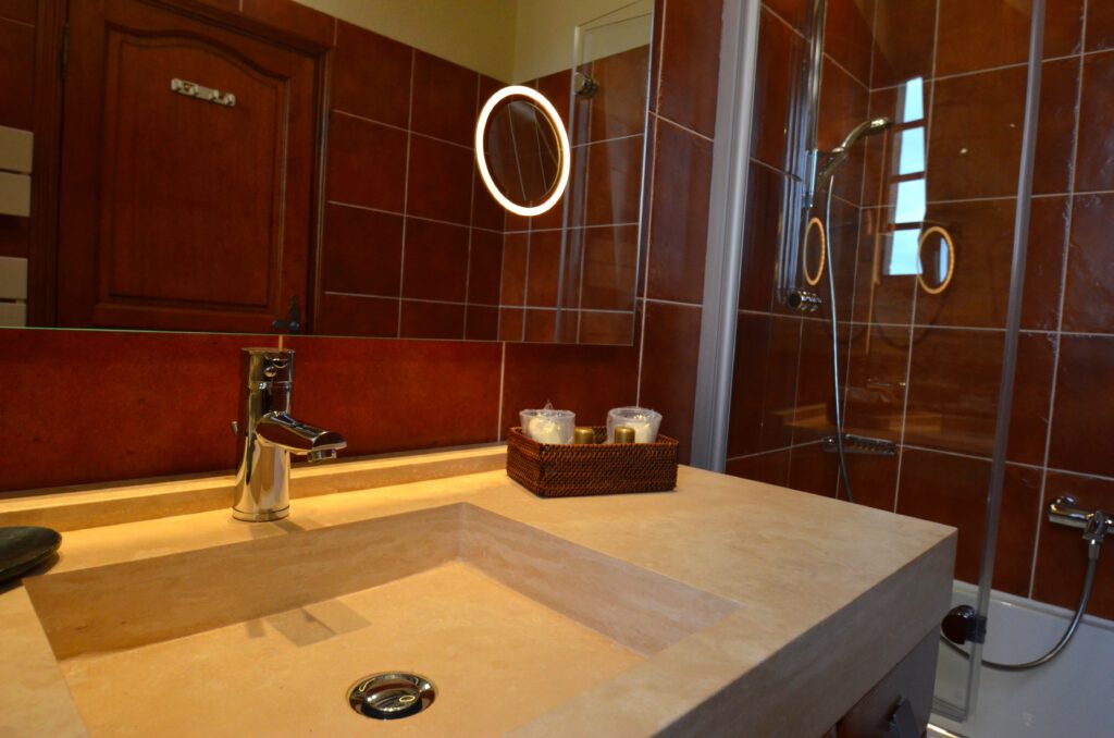 Baño moderno con fregadero de piedra, toque cromado y productos de belleza en una canasta. Mundial en azulejos en marrón.