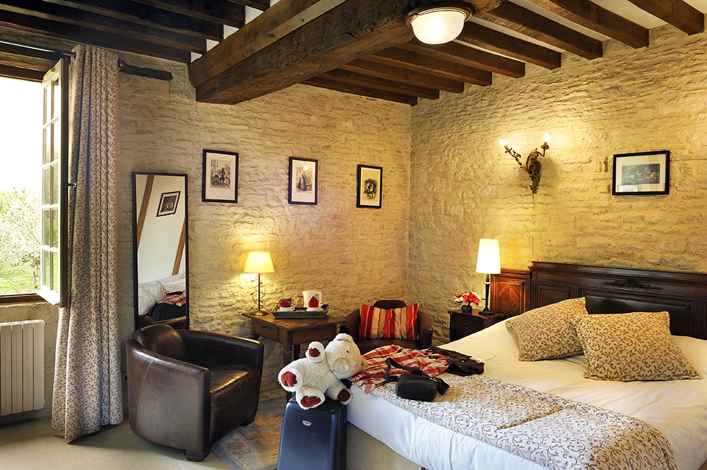 Habitación cómoda en el Mathan Manor, con cama, sillón, decoración de piedra y luz natural.