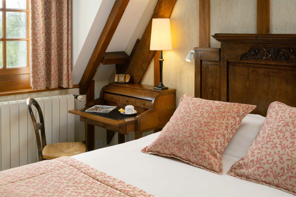 Elegante Sala Mathan Manor, che combina comfort moderno e fascino storico, con letto, scrivania in legno e luce morbida.